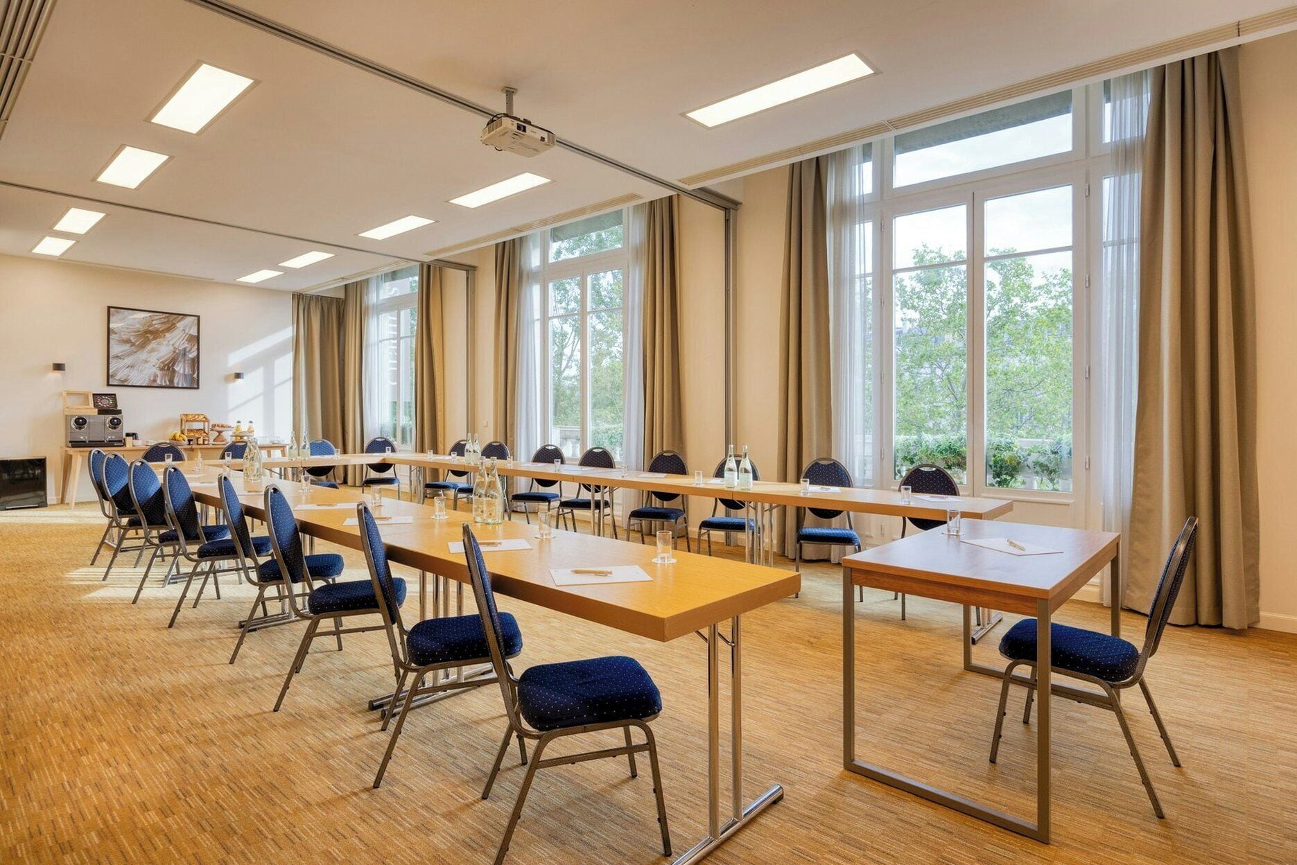 A conference room with long tables, chairs, a projector, and large windows.