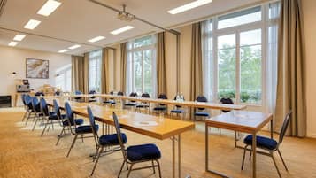 Une salle de conférence équipée de longues tables, de chaises, d’un projecteur et de grandes fenêtres.