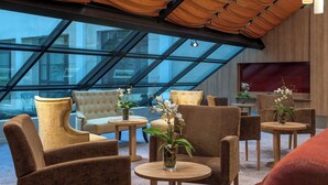 Un espace détente moderne doté d’un plafond en verre, de sièges confortables et de petites tables ornées de vases.