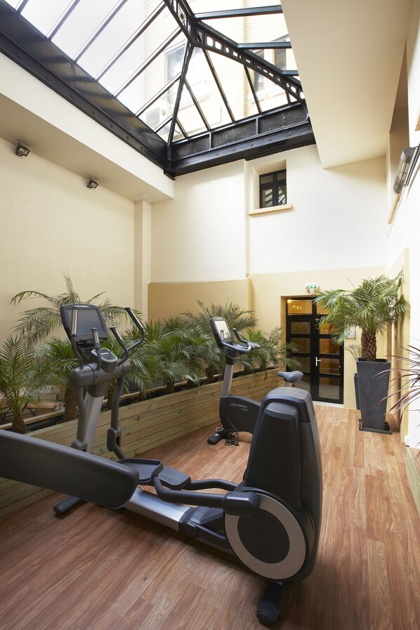 Une salle de sport intérieure équipée de matériel d’exercice, dotée d’un plancher en bois et agrémentée de plantes en pot.