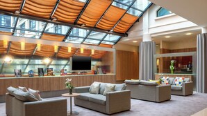 Un hall d’entrée spacieux avec un plafond haut, un atrium vitré et un mobilier moderne.