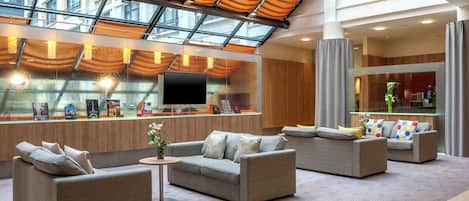 A spacious lobby with a high ceiling, a glass atrium, and modern furniture.