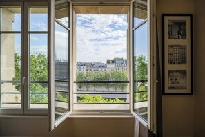 Habitación con un ventanal grande con vistas a un paisaje urbano, un cuadro en la pared y una barandilla de balcón.