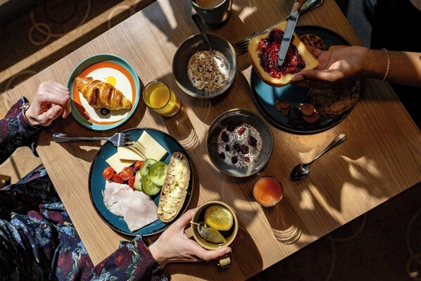 A wooden table with various breakfast items including croissants, cheese, ham, and bread.