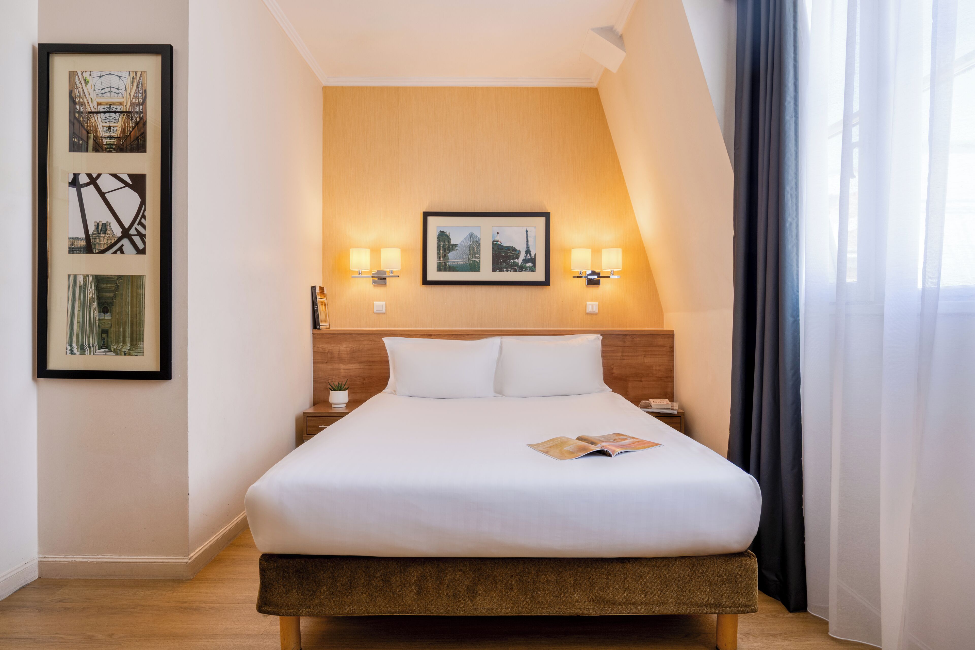 A hotel room with a large bed, two wall-mounted lamps, and framed pictures on the wall.