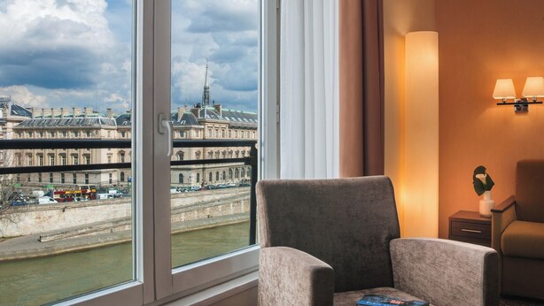 Une chambre d’hôtel dotée d’une grande fenêtre donnant sur un bâtiment historique et une rivière.