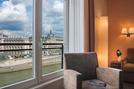 A hotel room with a large window offering a view of a historic building and a river.
