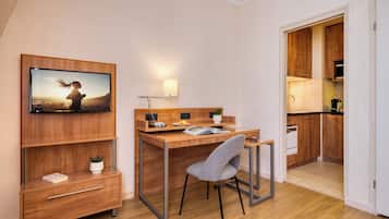 Een moderne slaapkamer met een houten bureau, een stoel, een aan de muur bevestigde televisie en een klein plantje op het nachtkastje.