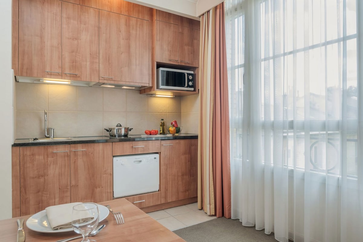 Cocina compacta con armarios de madera, microondas, lavavajillas y comedor con mesa para dos.