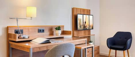 A modern hotel room with a wooden desk, a chair, a lamp, a television, and a potted plant.