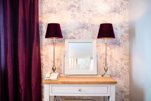 Une coiffeuse avec un miroir, deux lampes et un téléphone, le tout posé sur un comptoir en bois.