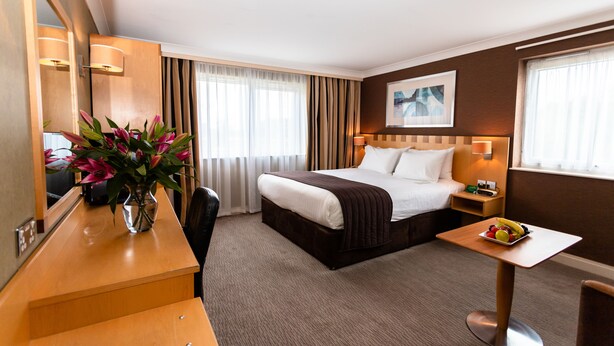 A hotel room with a bed, bedside table, desk, chair, and a vase of flowers. - Holiday Inn A55 Chester West by IHG (Deeside)