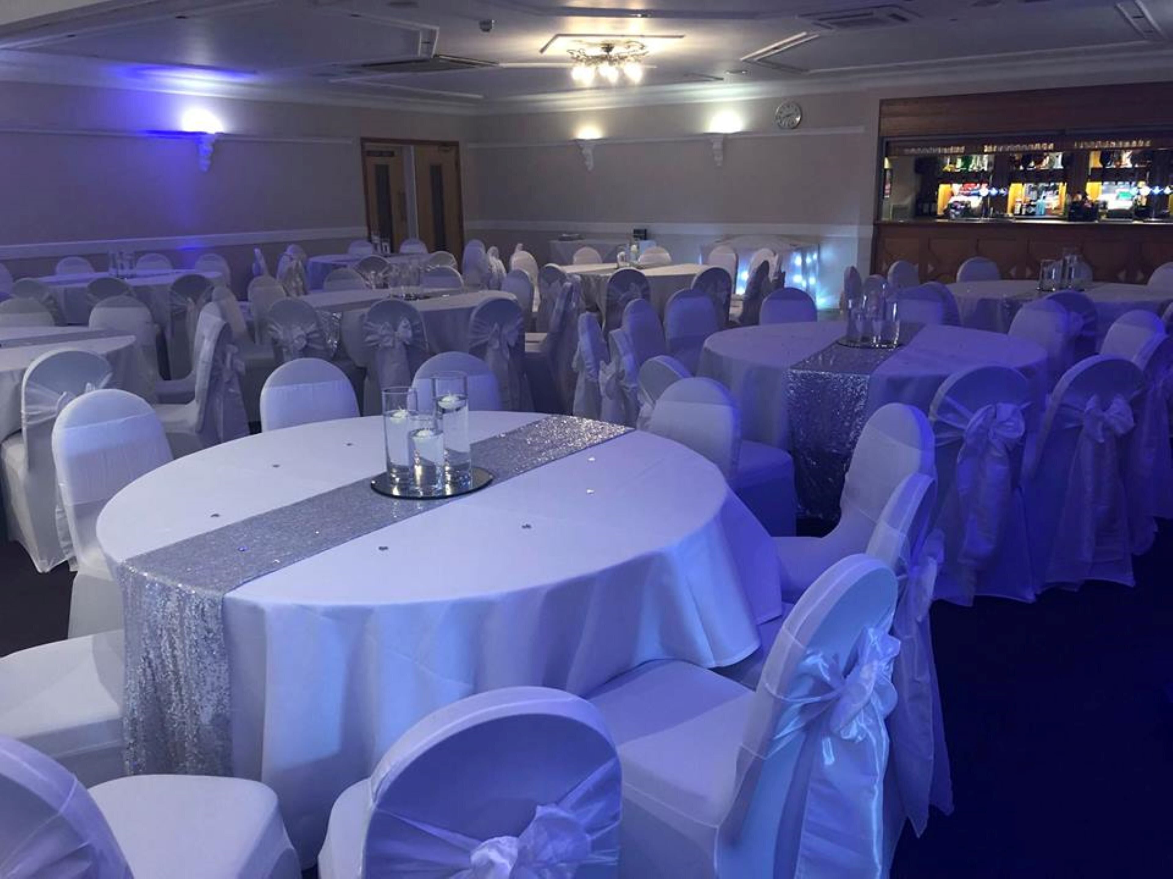 A banquet hall with round tables covered in white tablecloths and chairs with white sashes.