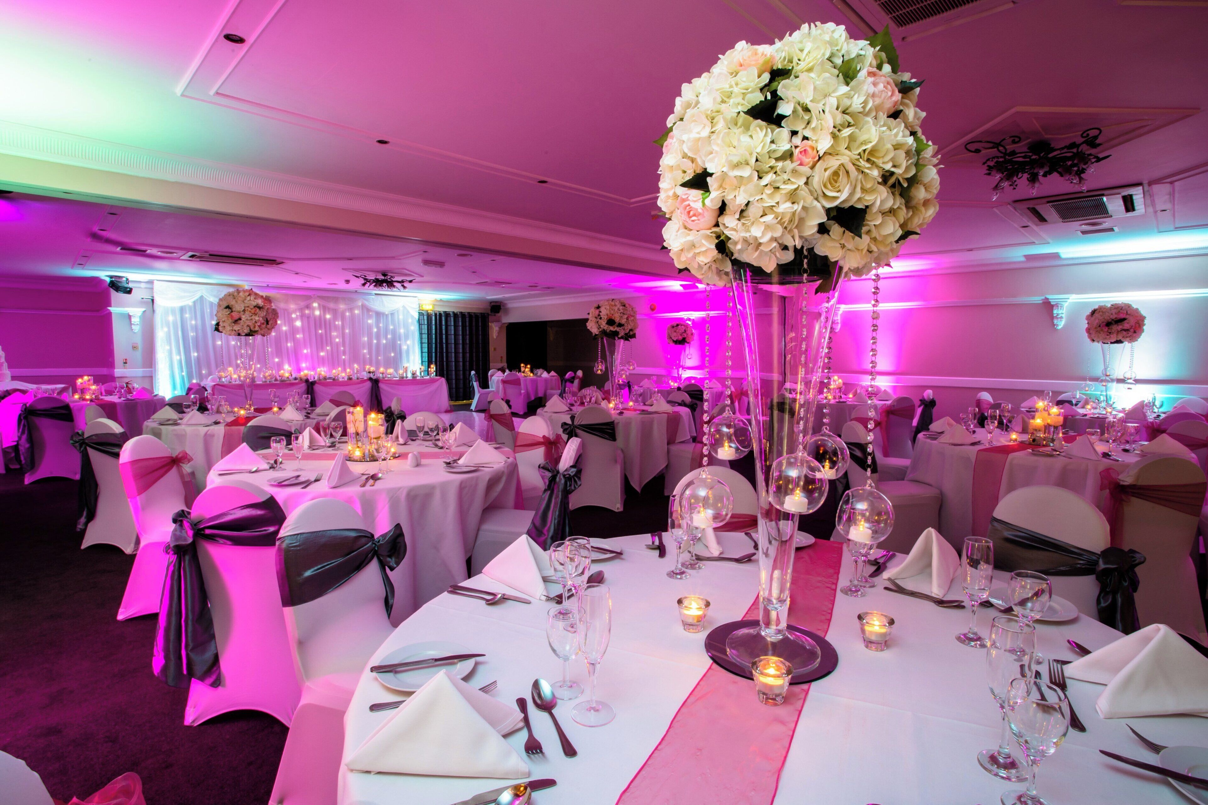 A banquet hall with round tables, white tablecloths, and chairs with black sashes.