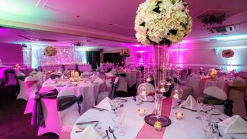 A banquet hall with round tables, white tablecloths, and chairs with black sashes.