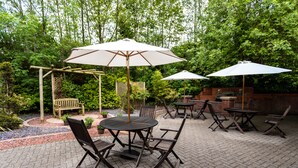 An outdoor patio area with tables and chairs, surrounded by greenery and a brick wall. - Holiday Inn A55 Chester West by IHG (Deeside)