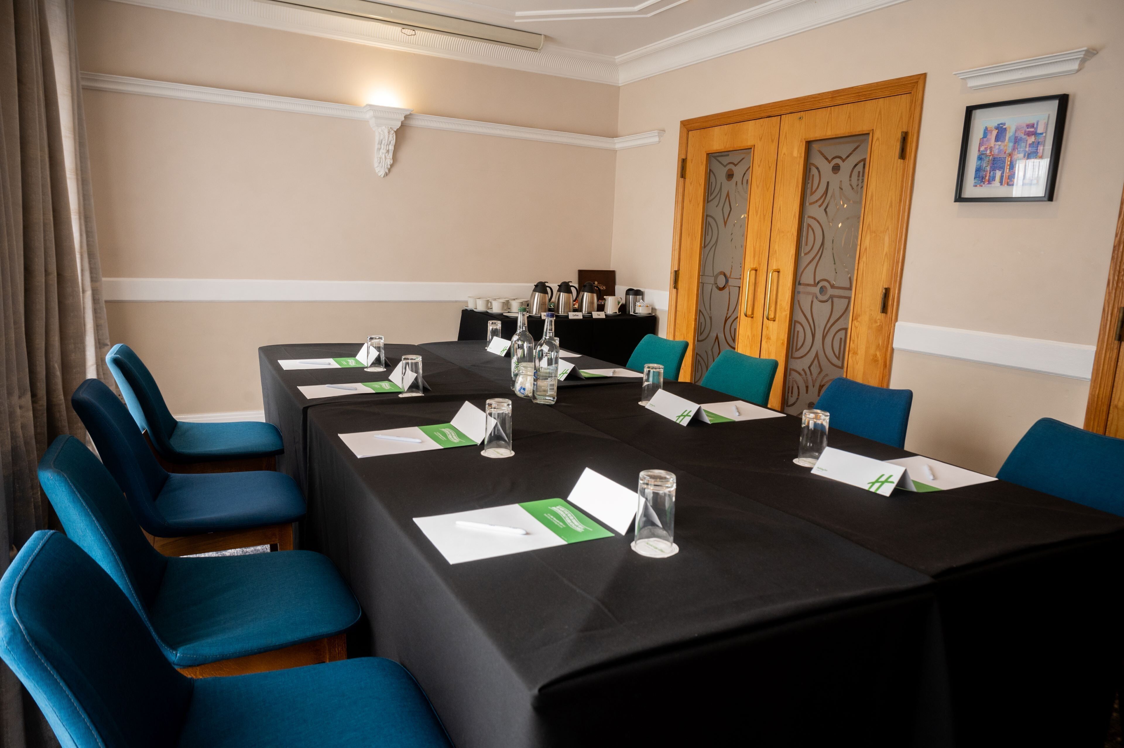 A conference room with a long table, blue chairs, name cards, and a black tablecloth.