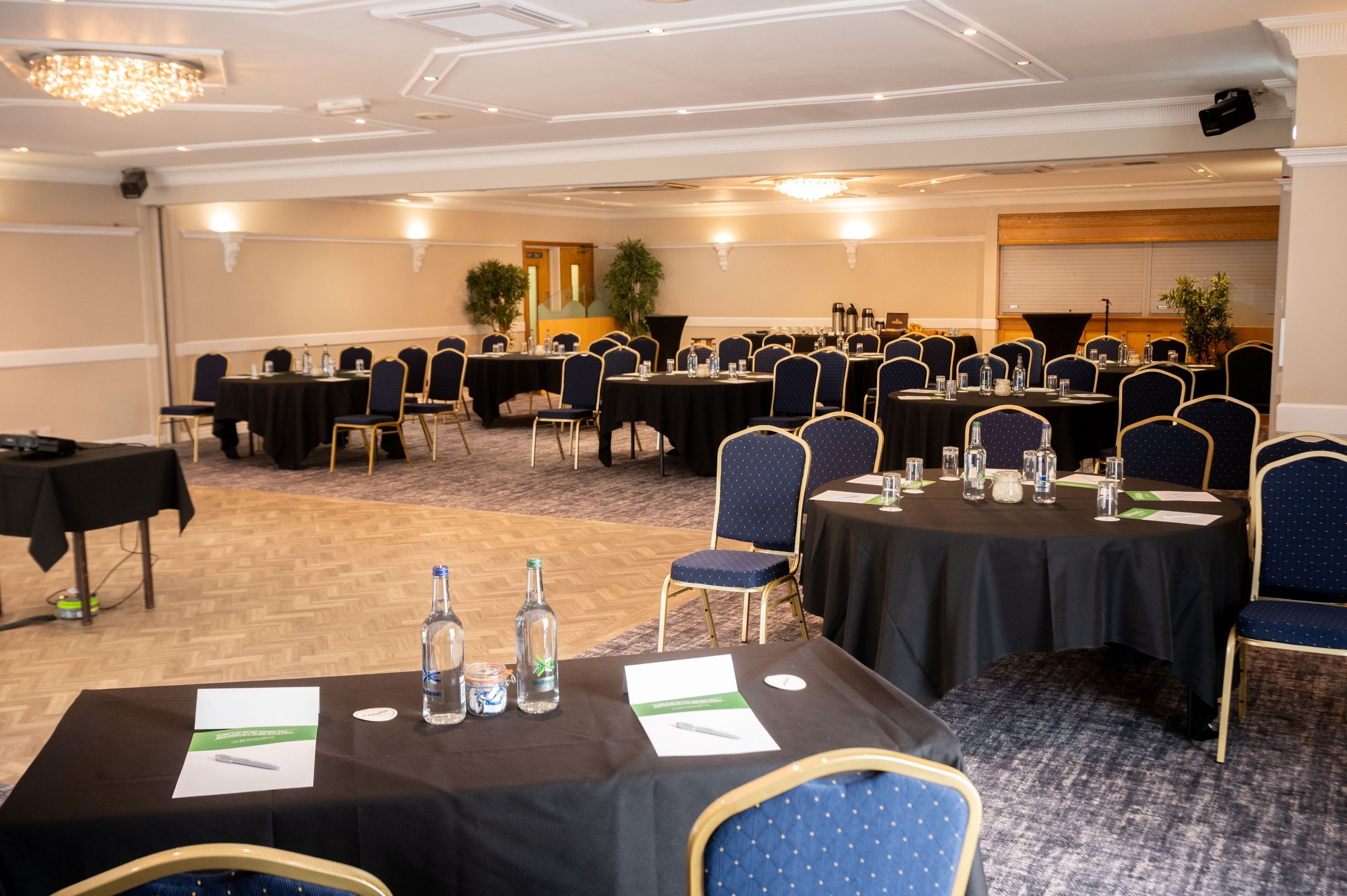 A conference room with multiple tables set up for meetings, equipped with chairs and tables, and a carpeted floor.
