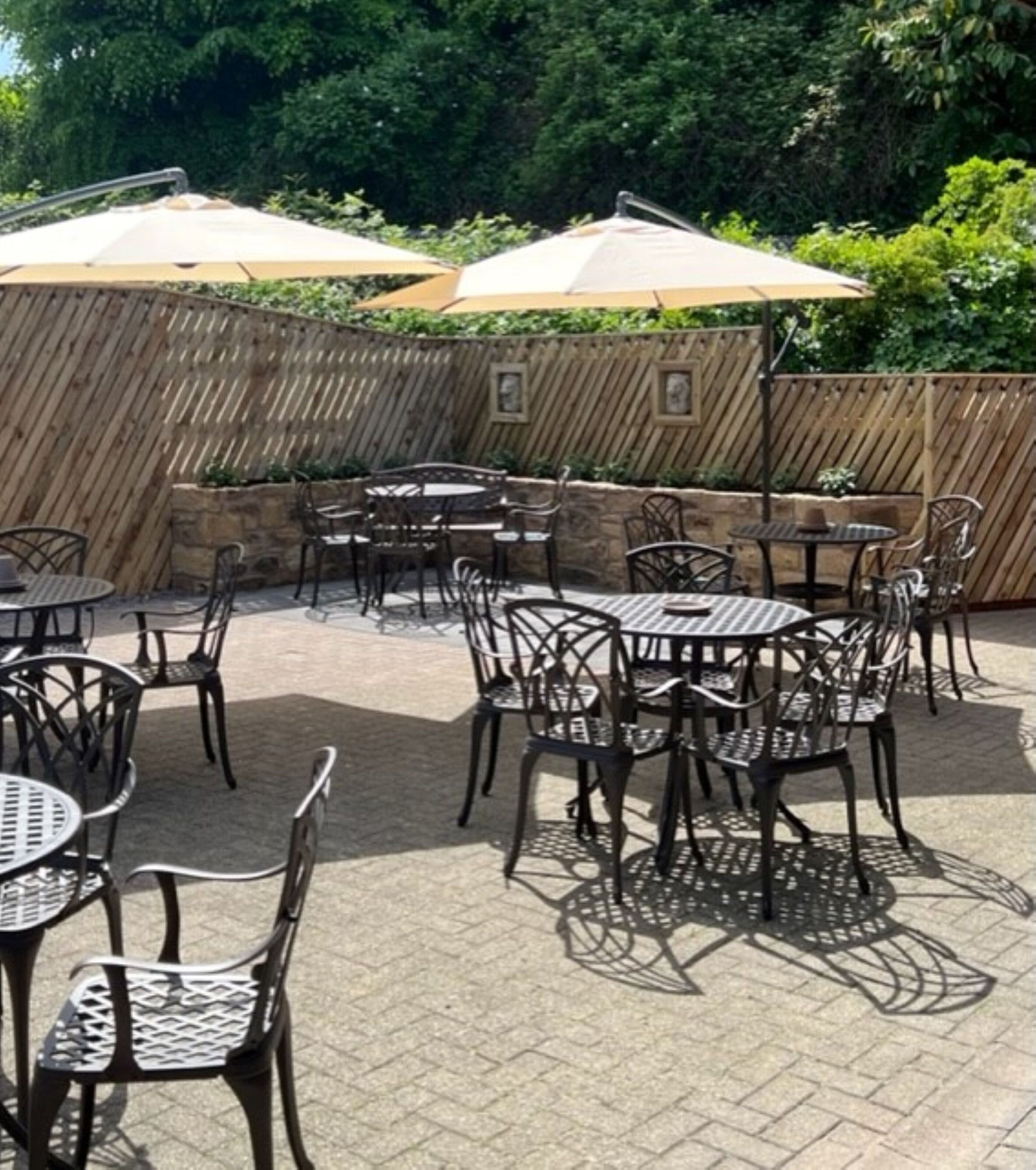 An outdoor patio area with round tables and chairs, surrounded by a wooden fence and greenery.