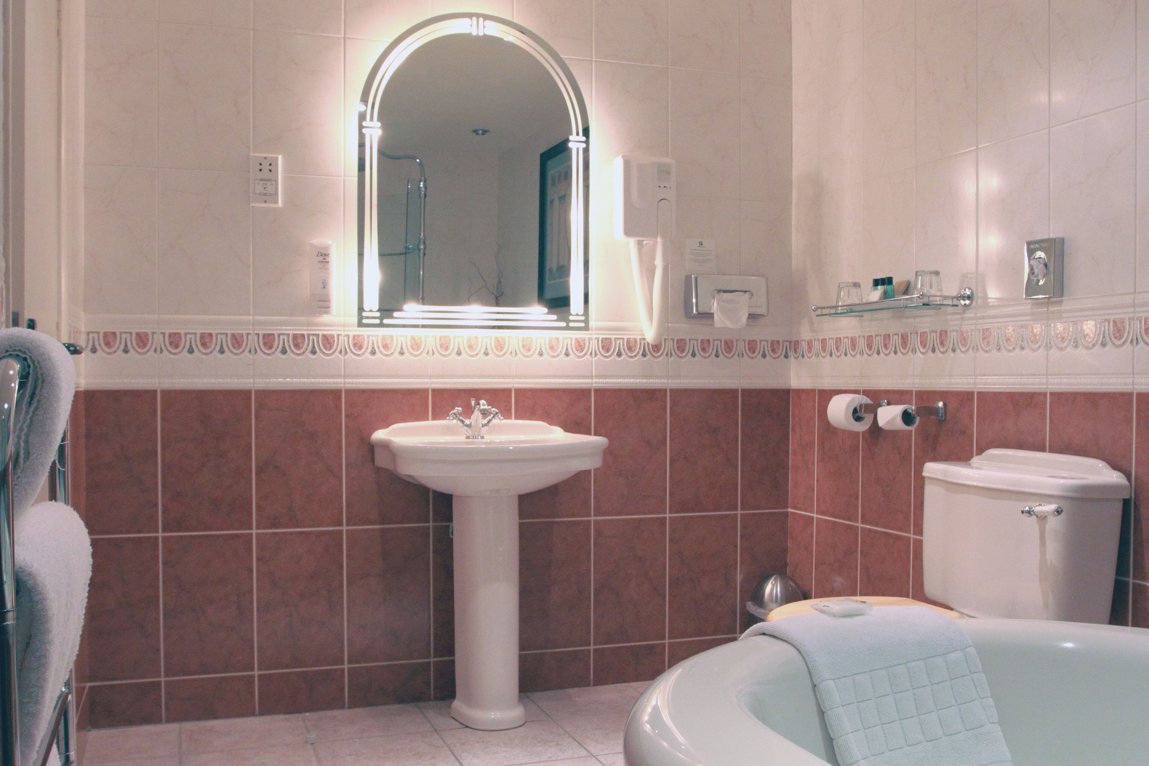 Et badeværelse med et håndvaskarrangement, et spejl, et toilet og et badekar.