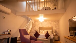 A hotel room with a loft area, a bed with multiple pillows, a chair, a desk with a kettle, and a nightstand with a lamp. - Holiday Inn A55 Chester West by IHG (Deeside)