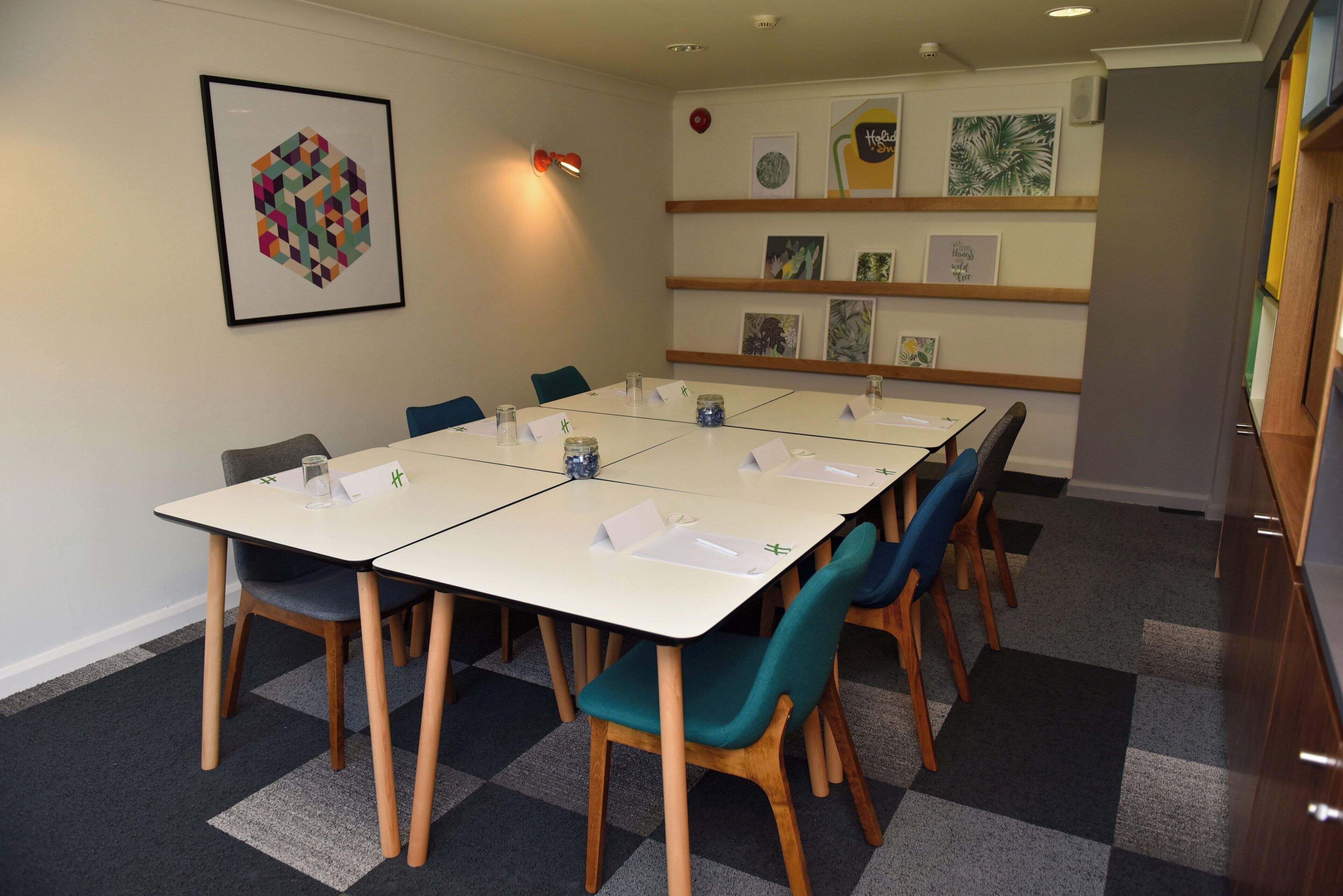 Un salón de conferencias con una larga mesa, sillas y una pared decorada con cuadros.