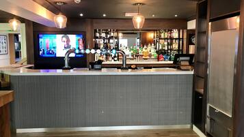 Zona de bar con mostrador, varias llaves, una pantalla de televisión y estantes llenos de botellas.