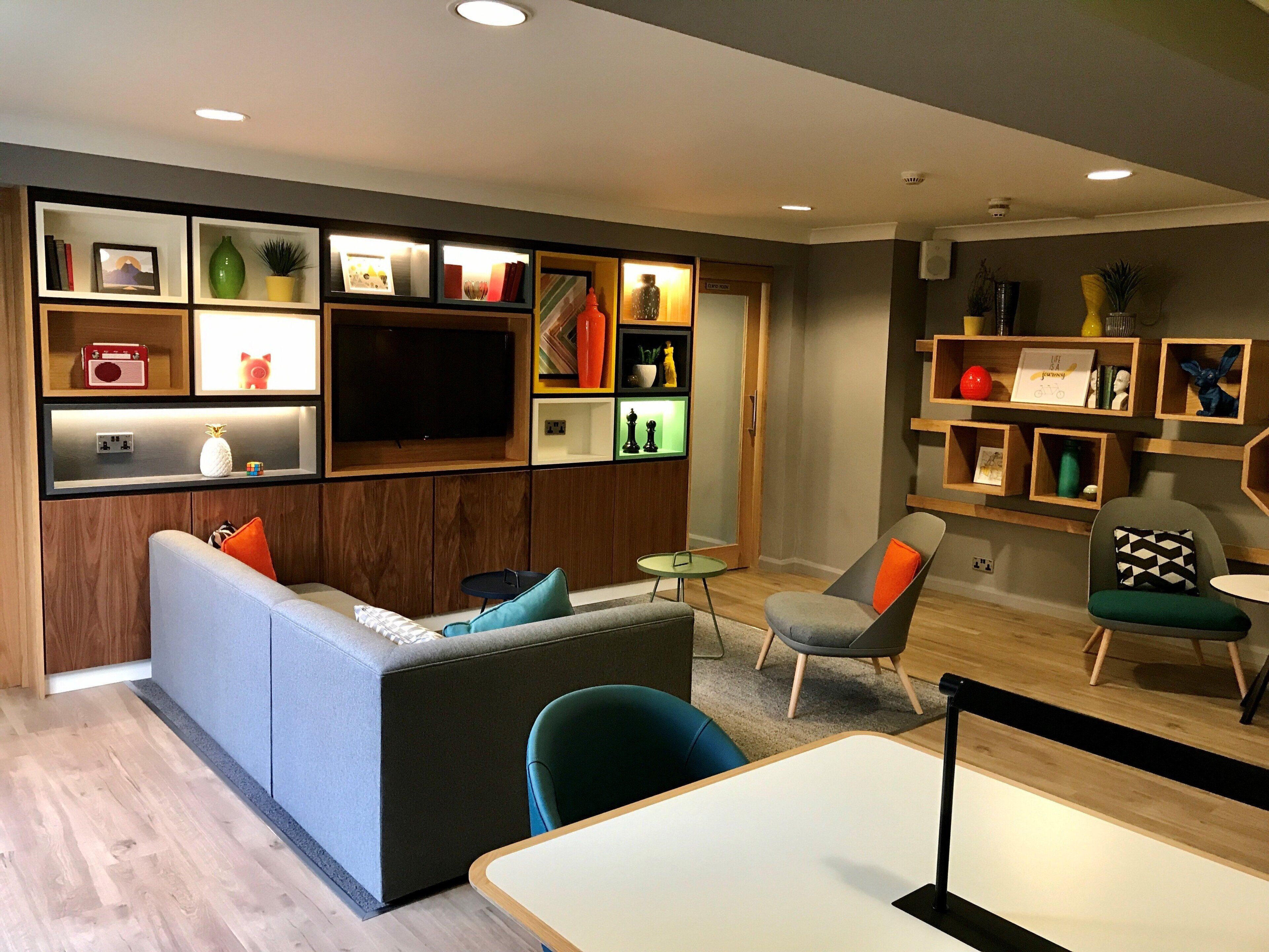 A modern living room with a sofa, chairs, a TV, and shelves with various items.