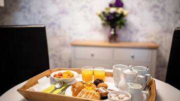 Un plateau de petit-déjeuner avec des croissants, des fruits et du jus, posé sur une table agrémentée de tasses blanches et d’un vase de fleurs en arrière-plan.
