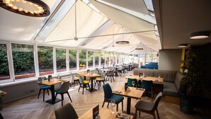 A restaurant with large windows, wooden tables, and chairs. - Holiday Inn A55 Chester West by IHG (Deeside)