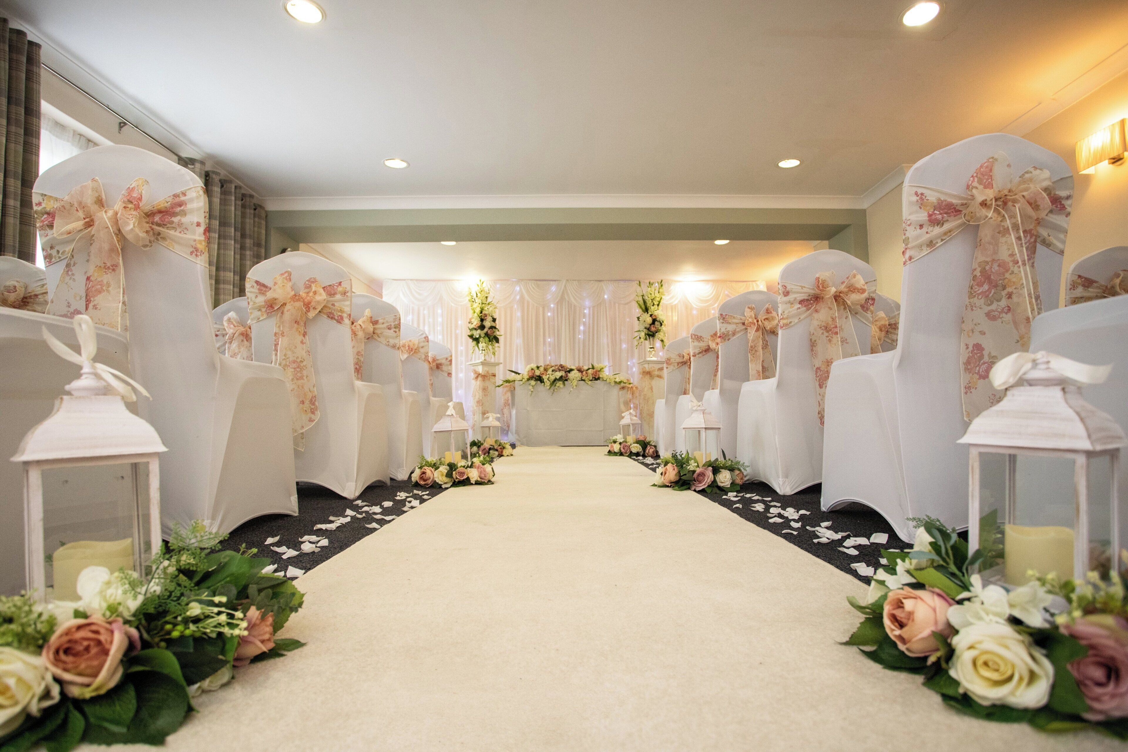 An aisle with chairs adorned with floral bows, white lanterns, and a carpeted floor.