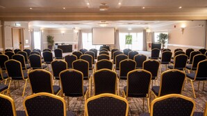 A conference room with rows of chairs, a projector screen, and a podium. - Holiday Inn A55 Chester West by IHG (Deeside)