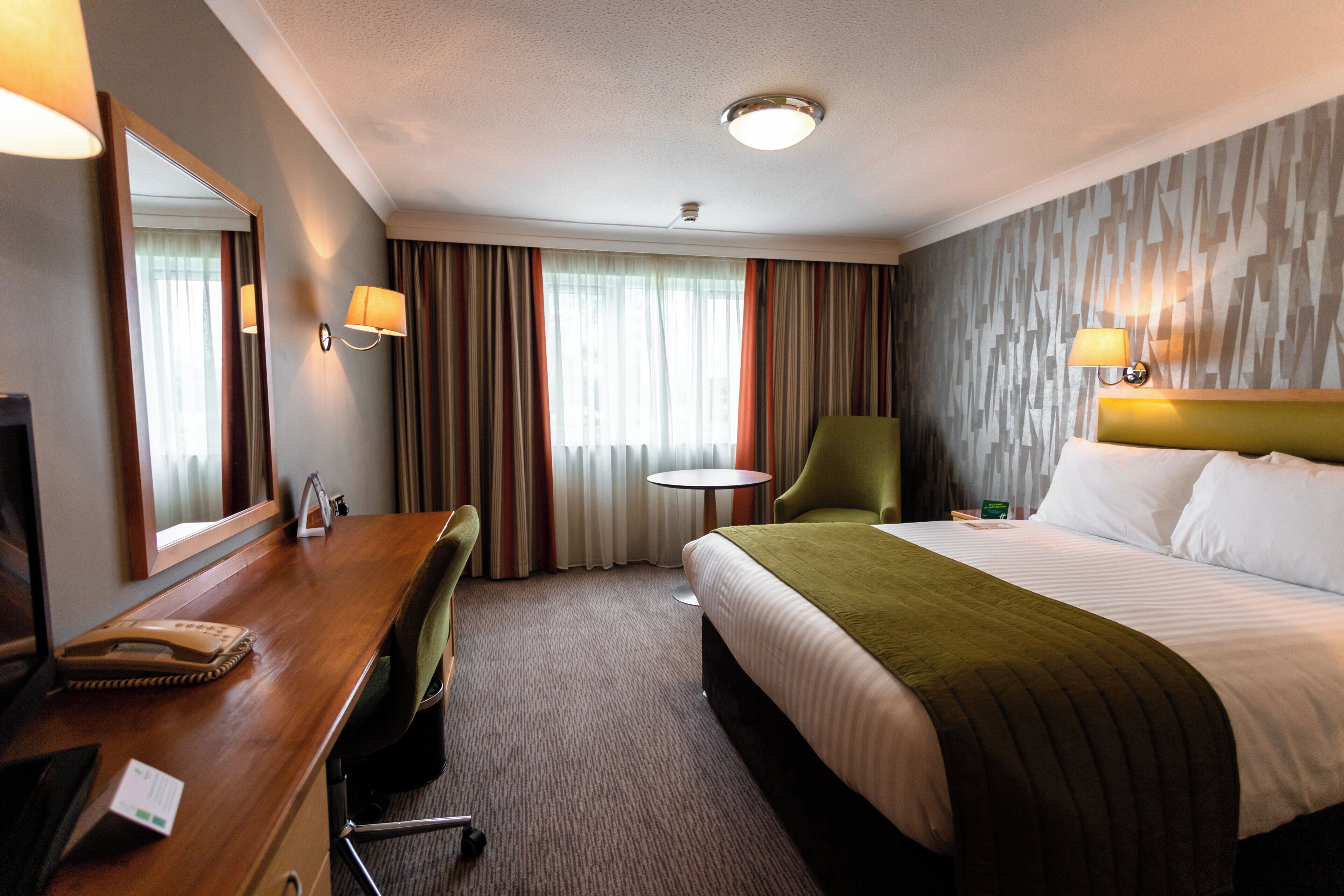 A hotel room with a bed, desk, chair, and a small table.