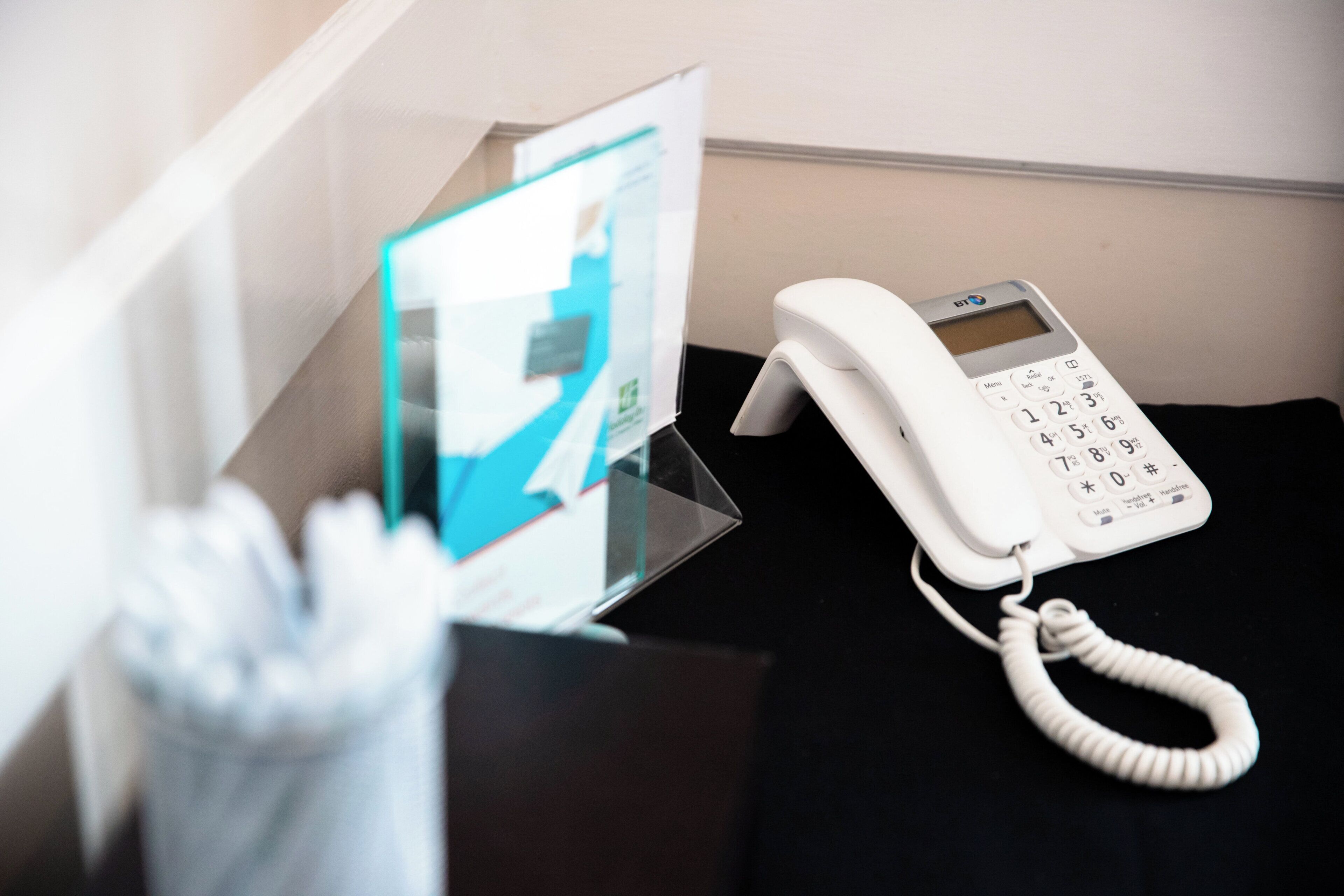Un téléphone blanc posé sur une surface noire, peut-être un bureau, avec une vitrine en arrière-plan.
