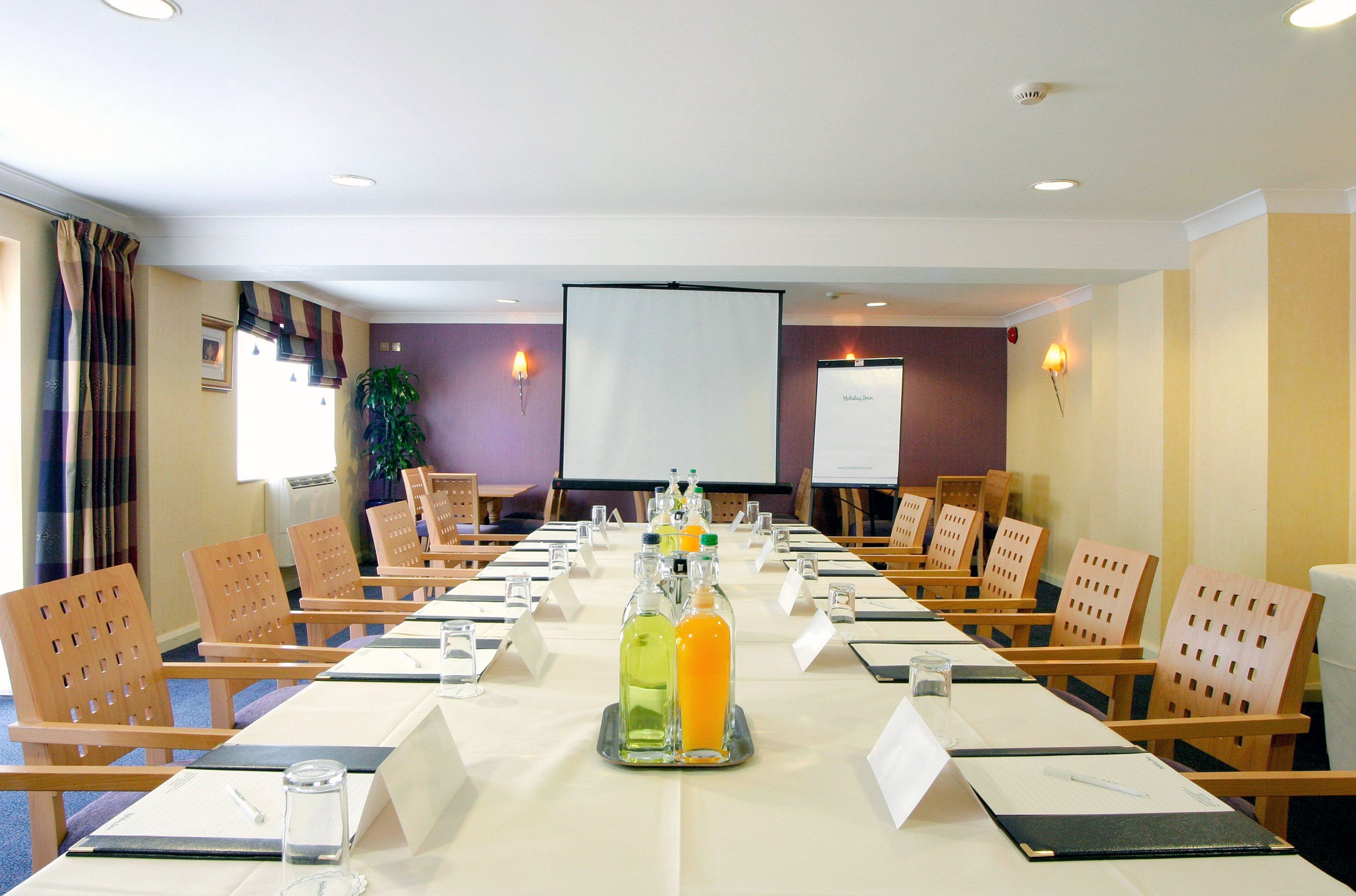 Une salle de conférence équipée d’une longue table, de chaises, de plaques nominatives et d’un écran de projection.