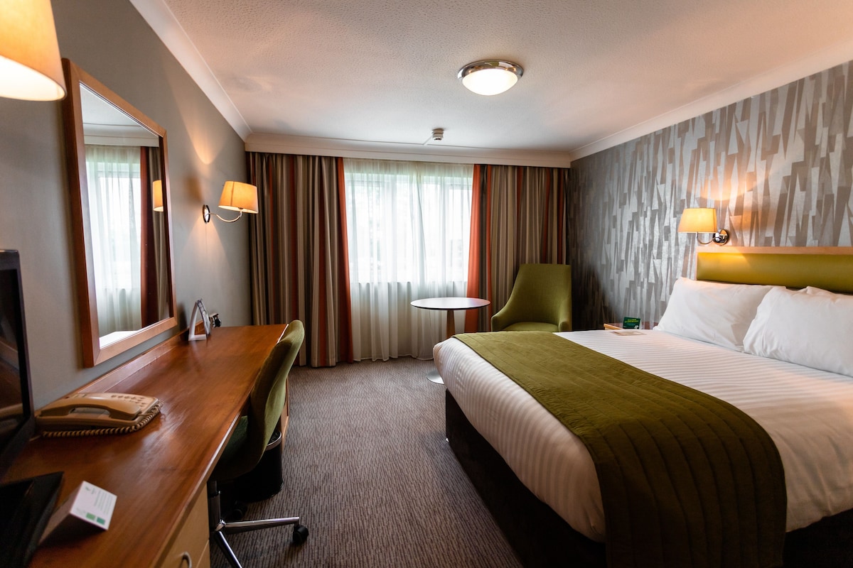 A hotel room with a bed, a desk with a telephone, a chair, a small table, and a mirror.