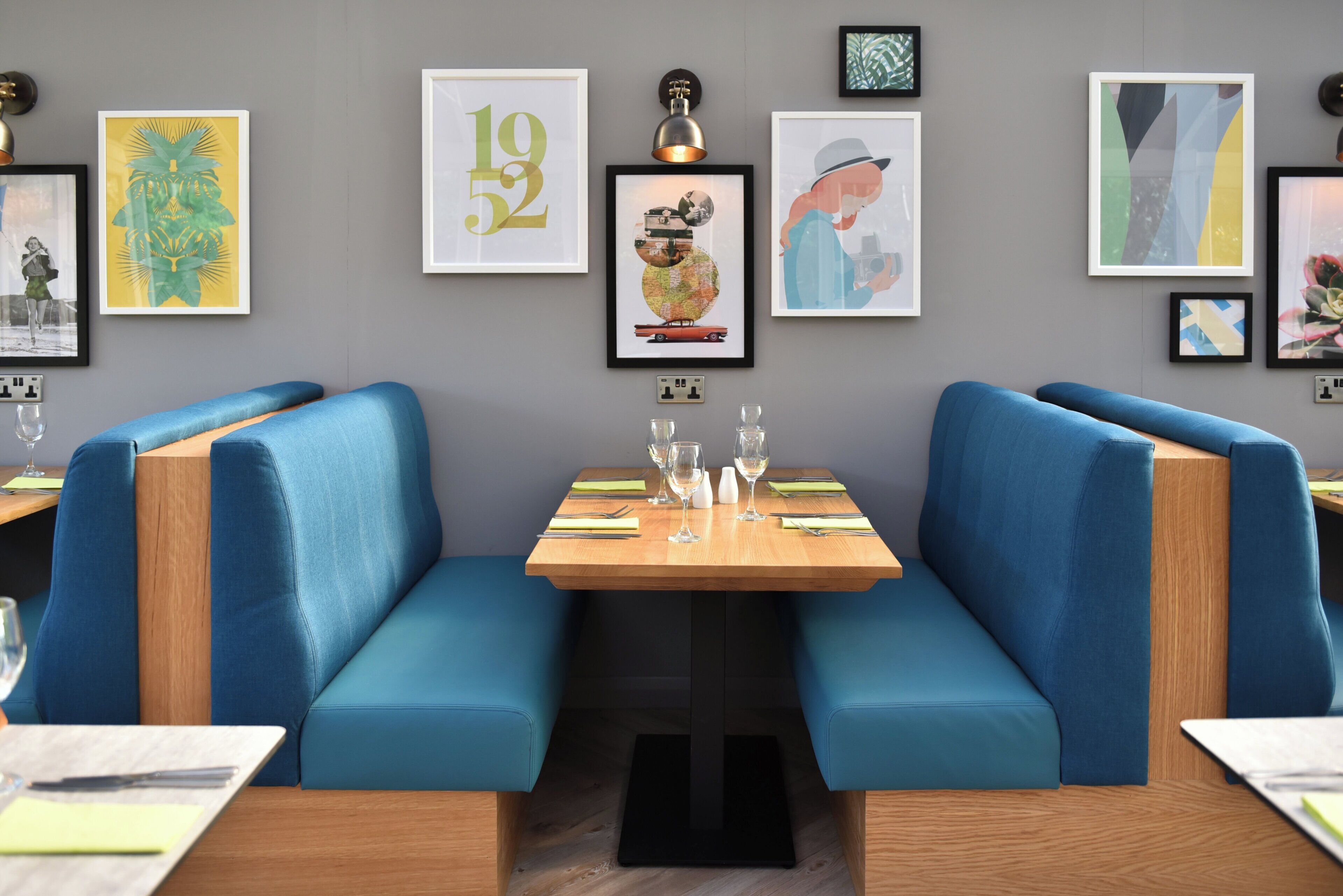 Un restaurant avec des banquettes bleues, une table en bois et divers tableaux encadrés accrochés au mur.