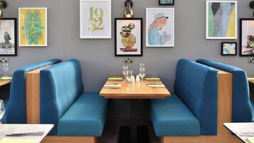 Un restaurant avec des banquettes bleues, une table en bois et divers tableaux encadrés accrochés au mur.