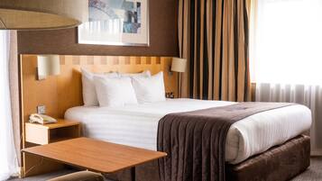 A hotel room with a large bed, a bedside table, a lamp, a phone, and a window with curtains.