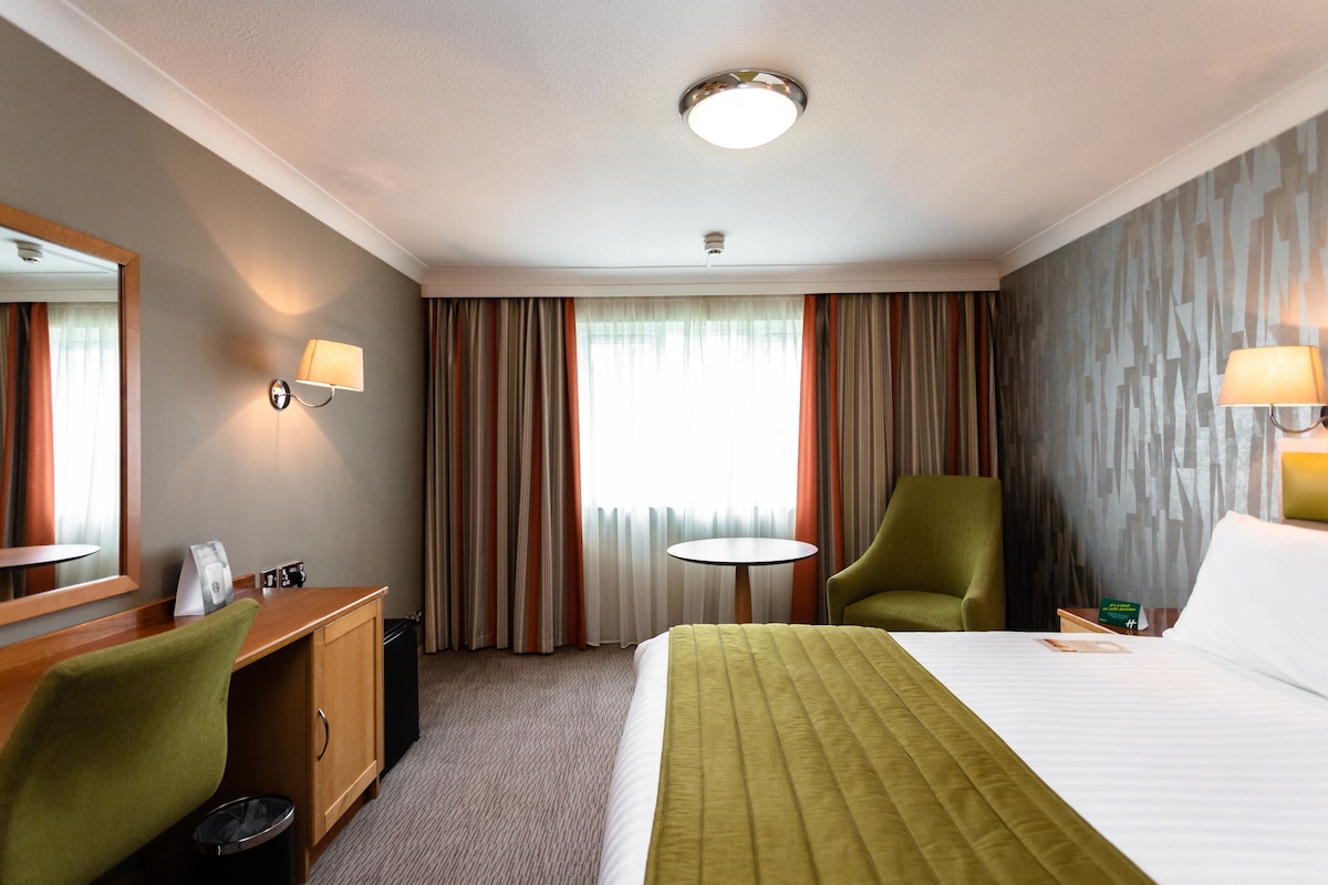 A hotel room with a bed, a desk, a chair, a round table, and a mirror.