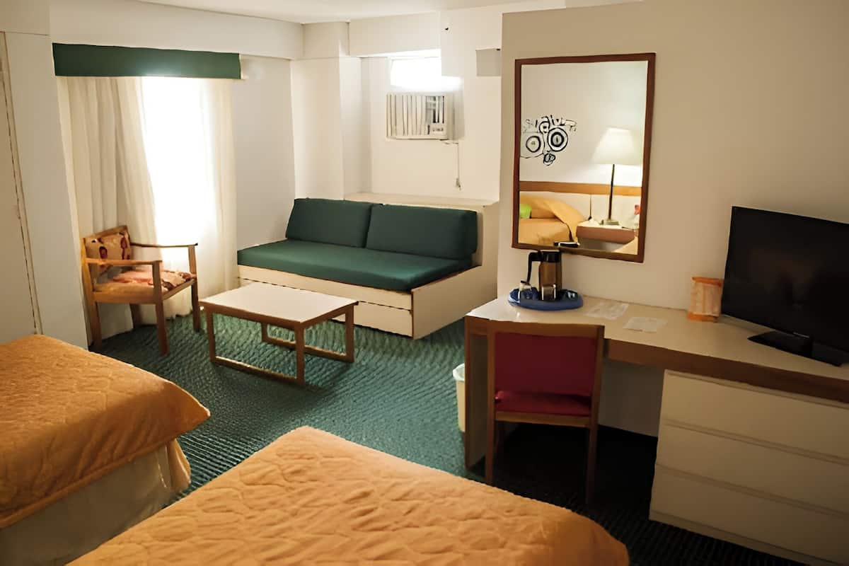 Hotelkamer met twee bedden, een bank, een bureau, een televisie, een spiegel en een raam met gordijnen.
