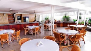 A restaurant with wicker chairs and round tables, a counter with a menu, and potted plants. - Caracas Cumberland  (Caracas)