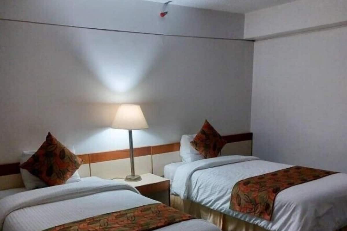 Een hotelkamer met twee bedden, een nachtkastje, een lamp en een groen tapijt.