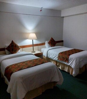 Quarto de hotel com duas camas, uma mesa de cabeceira, um abajur e um tapete verde.