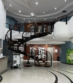 Un intérieur moderne avec un escalier en colimaçon, un comptoir d’accueil et une grande sculpture cylindrique blanche.