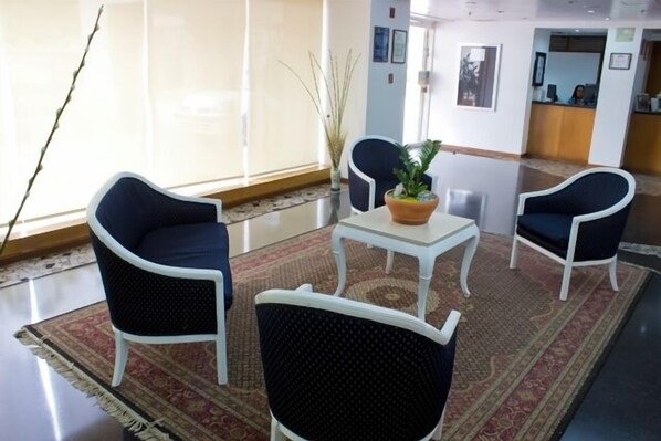 A lobby with two dark blue armchairs, a white coffee table, and a potted plant.