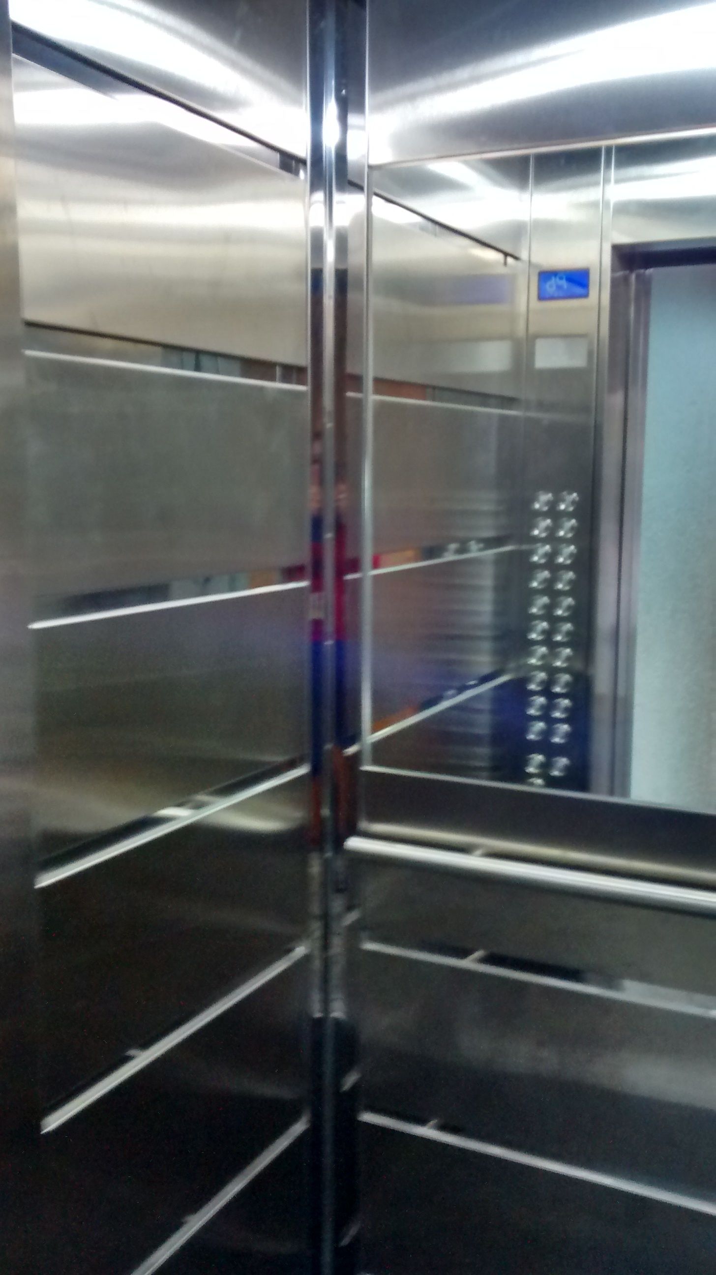A metallic elevator interior with reflective surfaces and a blue sign indicating the floor level.