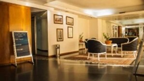 A modern hotel lobby with a reception desk, framed pictures on the wall, and a seating area with chairs and a table. - Caracas Cumberland  (Caracas)