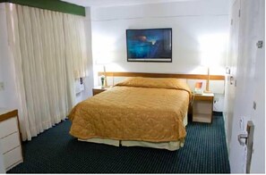 Une chambre d’hôtel avec un lit, une table de chevet, un tableau au mur et une fenêtre avec des rideaux.