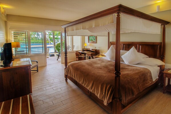 A four-poster bed with a brown bedspread, a desk with a lamp, and a chair in a hotel room with wooden floors and large windows. -  Plantation Bay a Real Resort with a Real Spa (Lapu-Lapu)